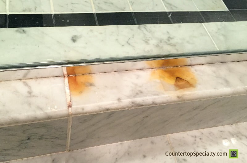 two orange rust stains on white carrara marble shower tile