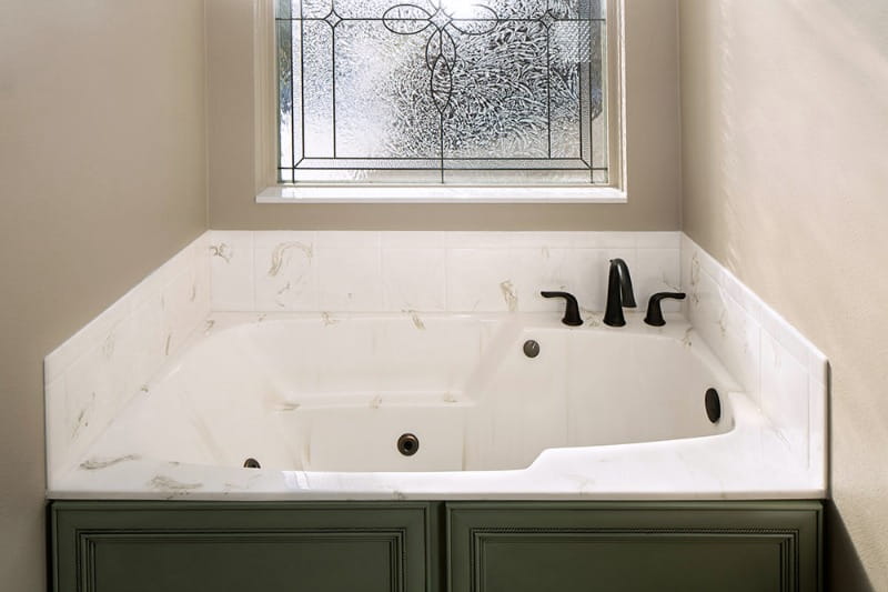 white cultured marble bathtub with jets under frosted window